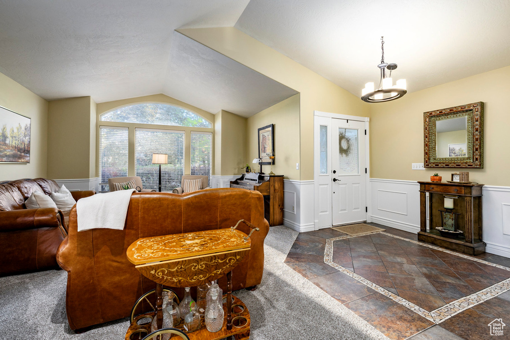 Foyer entrance with vaulted ceiling, inlaid floor details, wainscoting, and a chandelier