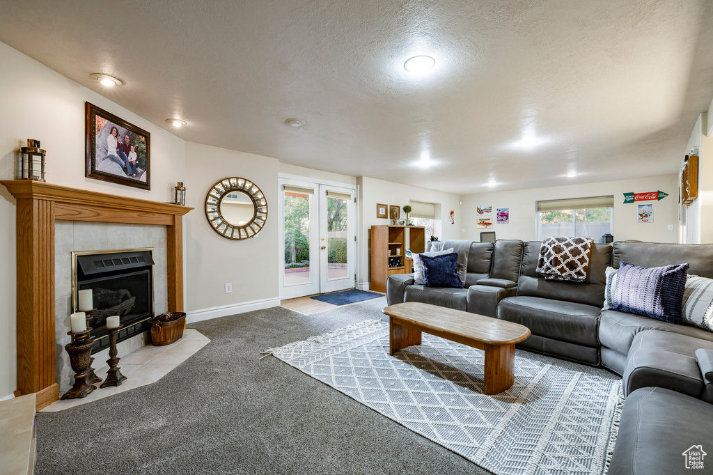 Carpeted living room featuring french doors, a tiled fireplace, baseboards, and a textured ceiling