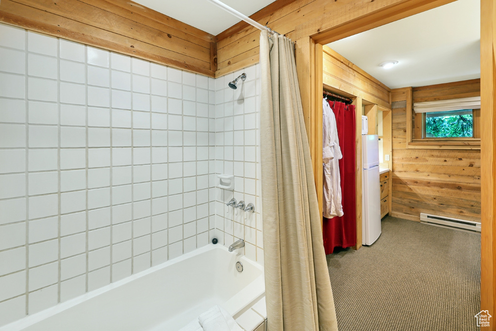 Bathroom with baseboard heating, shower / bath combination with curtain, and wooden walls