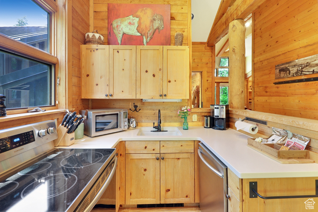 Kitchen featuring stainless steel appliances, wooden walls, a sink, light brown cabinets, and light countertops