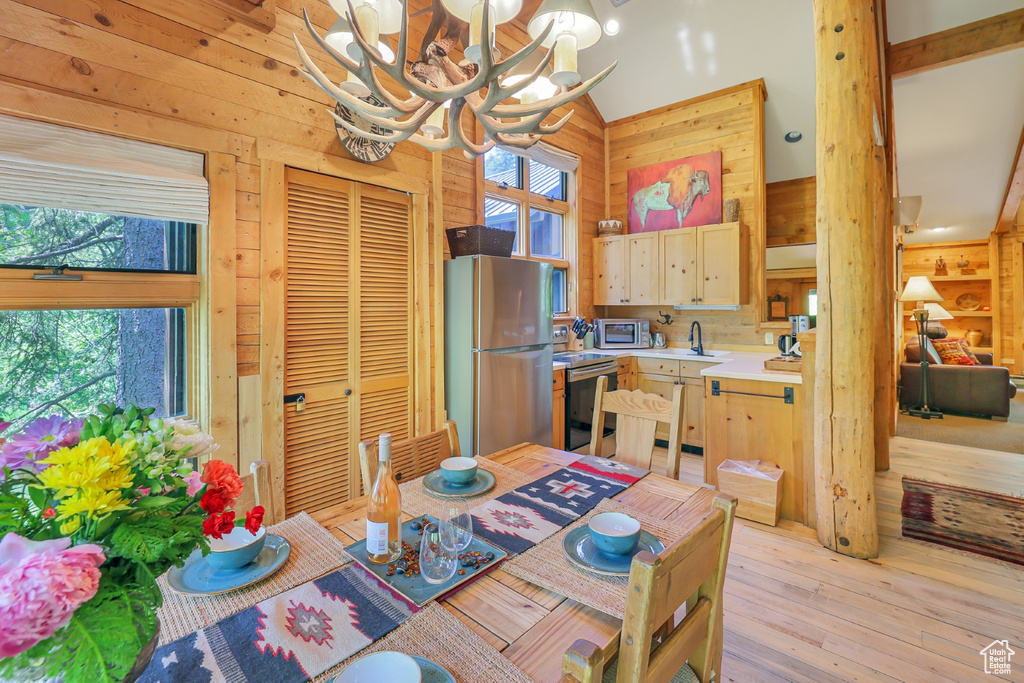 Dining space with wooden walls, a chandelier, light wood-type flooring, and lofted ceiling