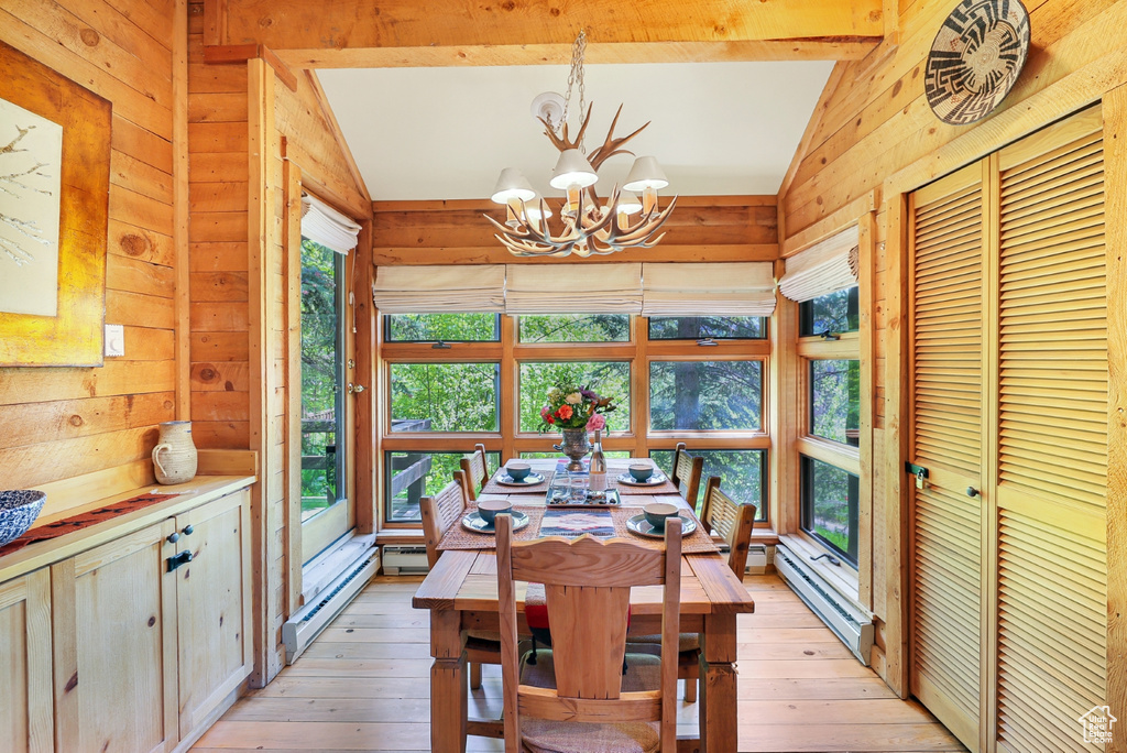 Dining room with wooden walls, a chandelier, a baseboard heating unit, light wood-style flooring, and baseboard heating