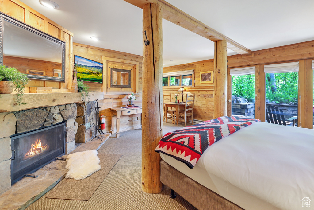 Carpeted bedroom featuring wooden walls, access to outside, and a stone fireplace