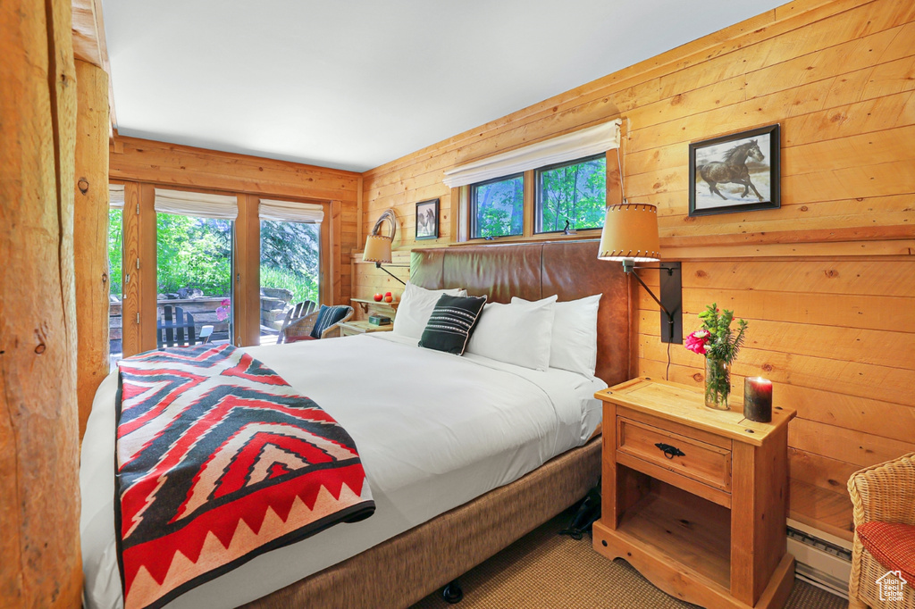 Bedroom featuring multiple windows, access to outside, wooden walls, carpet floors, and a baseboard heating unit