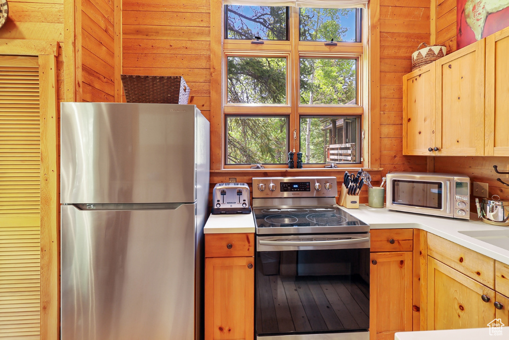 Kitchen featuring stainless steel appliances, wooden walls, and light countertops