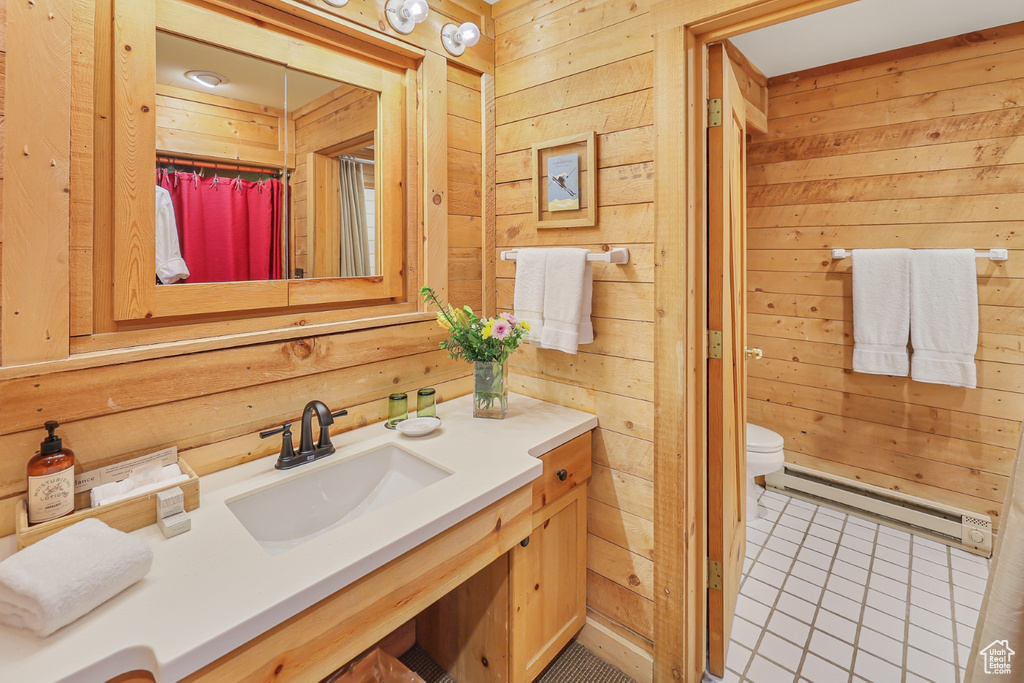 Full bathroom with wooden walls, baseboard heating, vanity, toilet, and tile patterned flooring