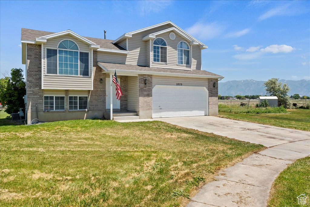Split level home featuring brick siding, concrete driveway, a front yard, and an attached garage