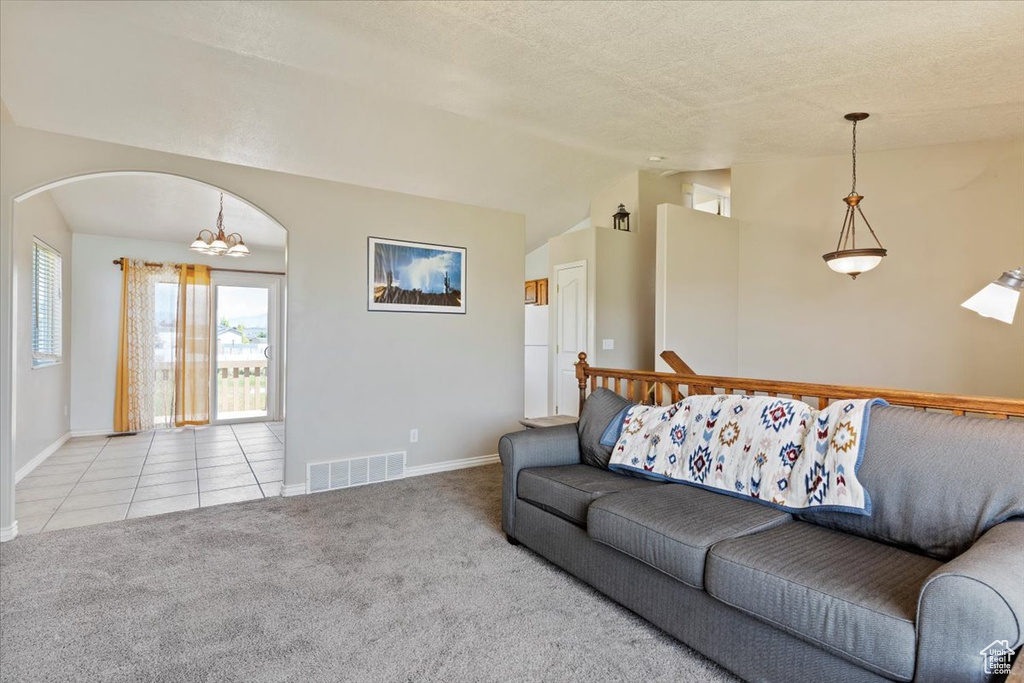 Tiled living room with vaulted ceiling, baseboards, carpet floors, a chandelier, and a textured ceiling