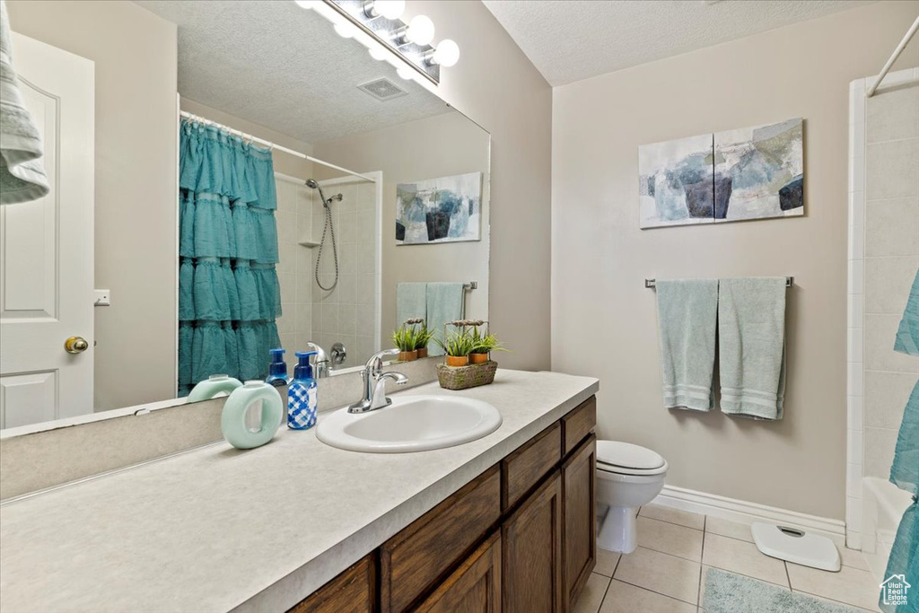 Full bathroom with vanity, toilet, tile patterned flooring, a textured ceiling, and baseboards