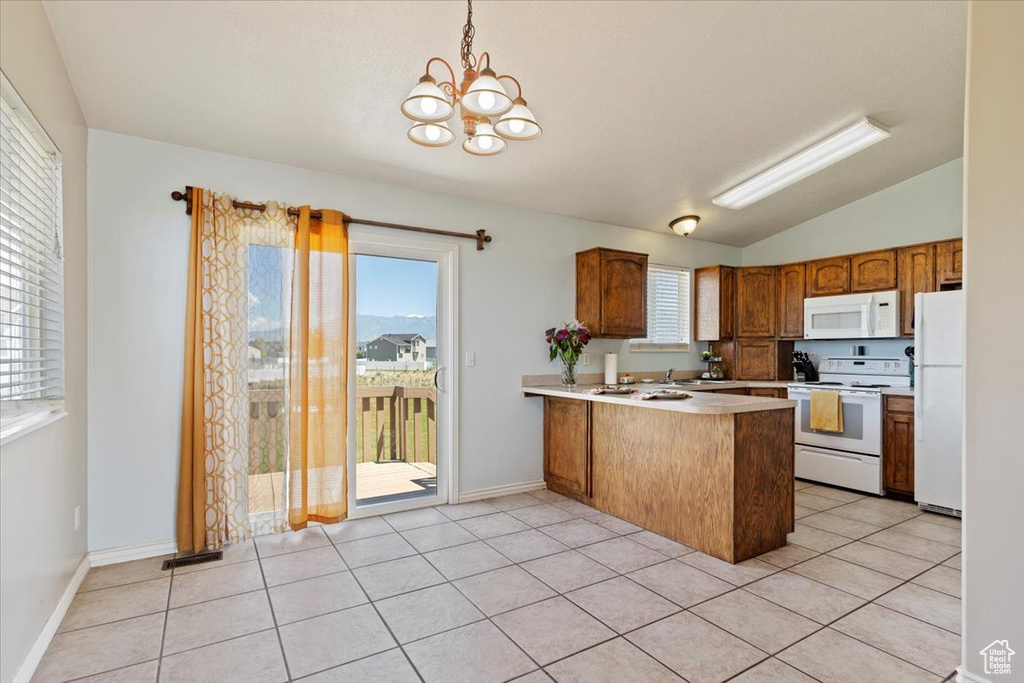 Kitchen with white appliances, a peninsula, a chandelier, vaulted ceiling, and light countertops