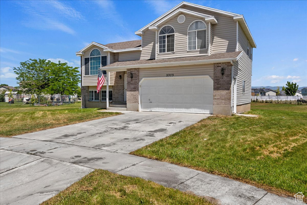 View of front of home with brick siding, concrete driveway, a front lawn, and a garage