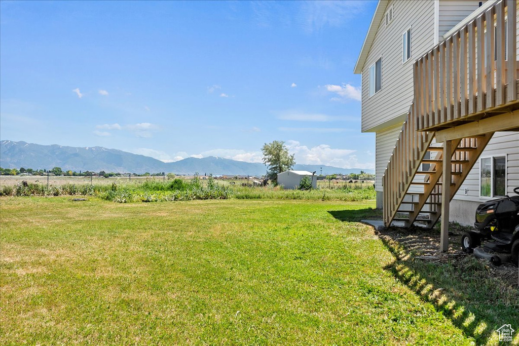 View of green lawn featuring stairs, a deck with mountain view, and a view of countryside