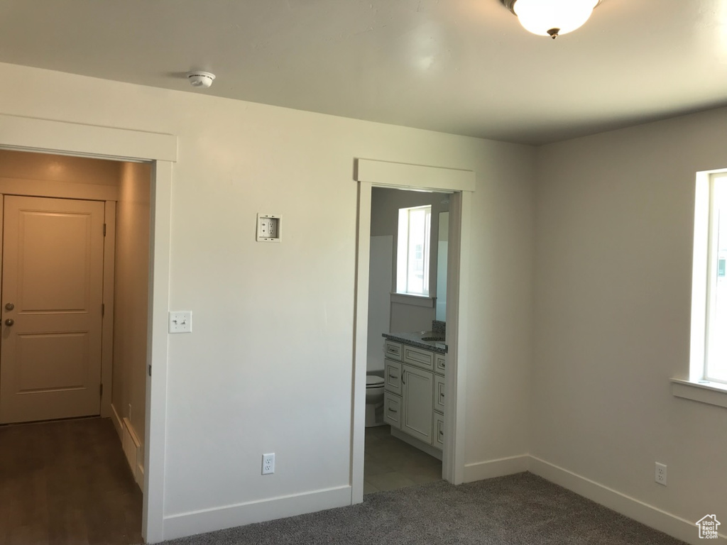 Unfurnished bedroom with baseboards, multiple windows, dark carpet, and ensuite bathroom