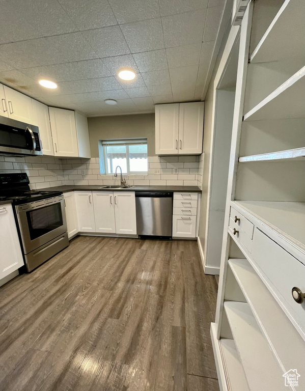 Kitchen featuring appliances with stainless steel finishes, a sink, open shelves, and white cabinetry