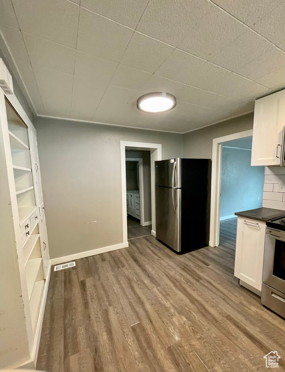 Kitchen with stainless steel appliances, dark countertops, wood finished floors, and white cabinetry