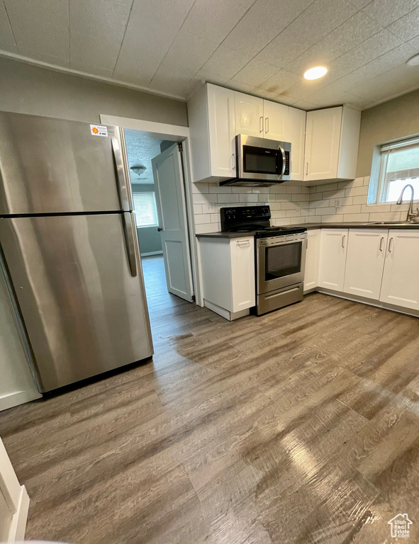 Kitchen featuring stainless steel appliances, dark countertops, white cabinetry, and wood finished floors
