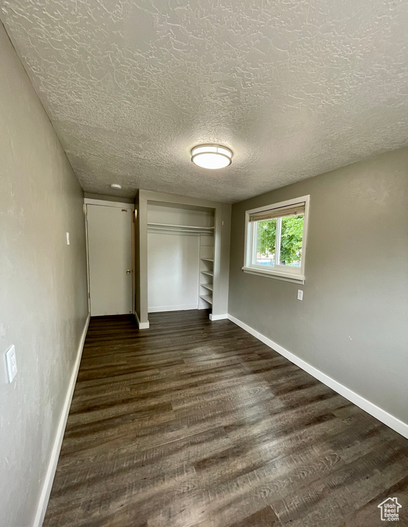 Unfurnished bedroom featuring baseboards, dark wood-type flooring, a textured ceiling, and a closet