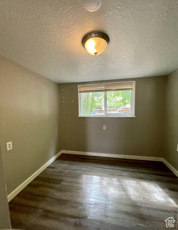 Spare room featuring wood finished floors, a textured ceiling, and baseboards