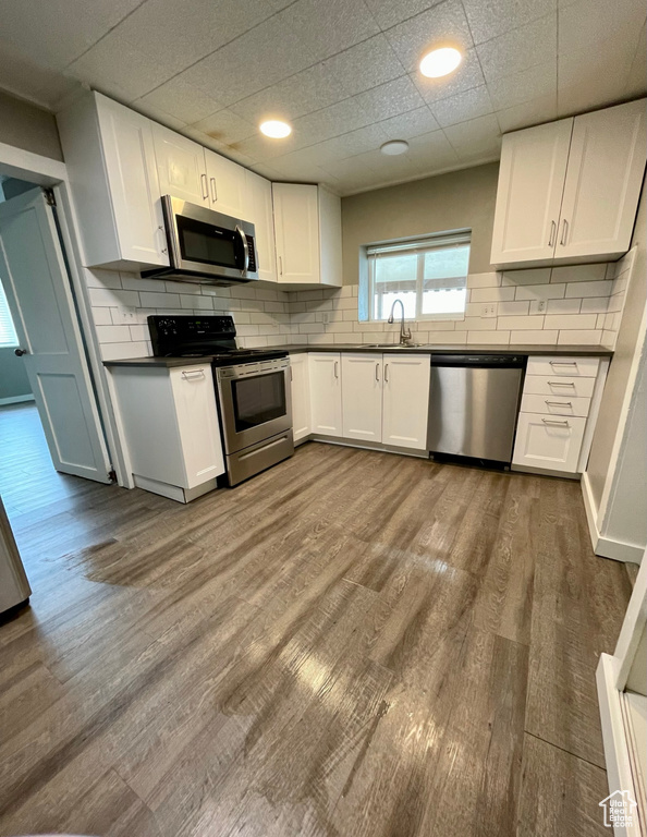 Kitchen featuring appliances with stainless steel finishes, dark countertops, white cabinets, and backsplash