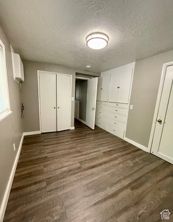 Unfurnished bedroom featuring dark wood finished floors, a textured ceiling, baseboards, and multiple closets