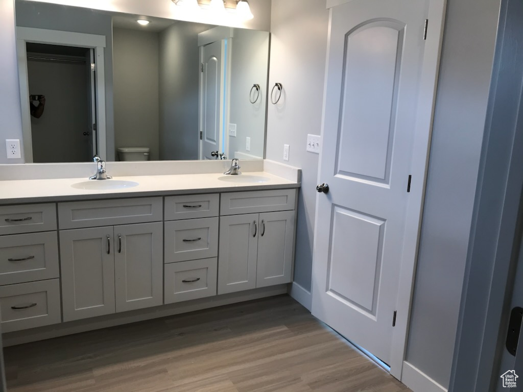 Full bath featuring double vanity, wood finished floors, toilet, and baseboards