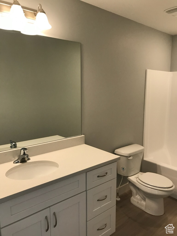Full bath featuring wood finished floors, toilet, vanity, and washtub / shower combination