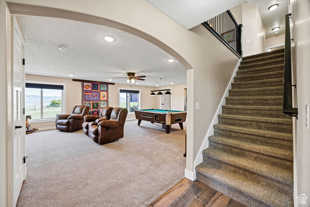 Rec room with arched walkways, a textured ceiling, carpet, baseboards, and a ceiling fan