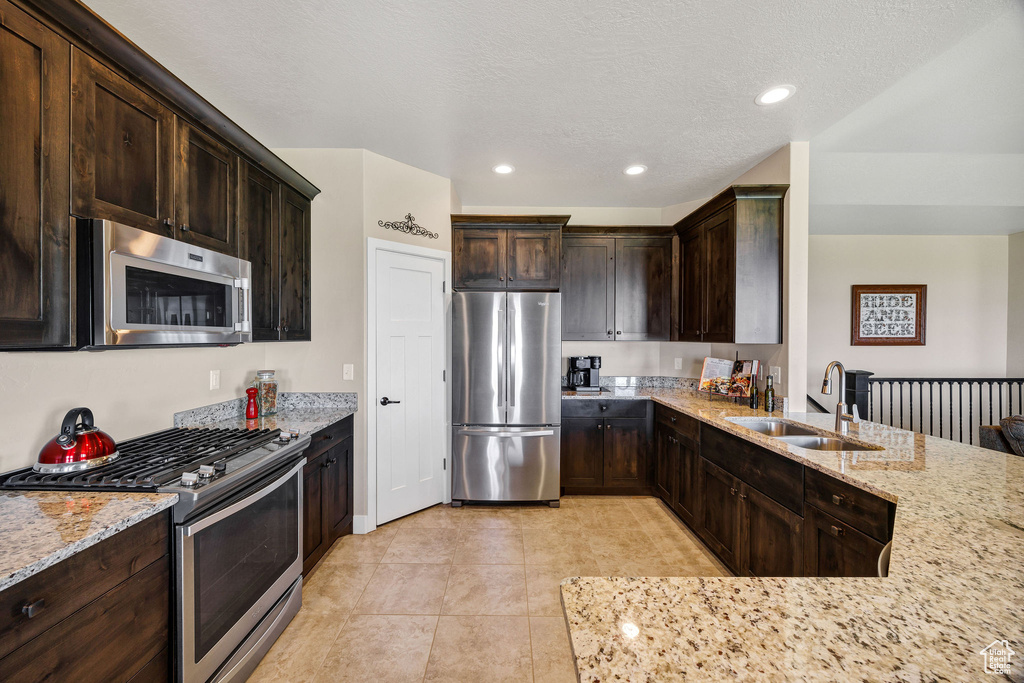 Kitchen with appliances with stainless steel finishes, light stone counters, dark brown cabinets, recessed lighting, and a peninsula