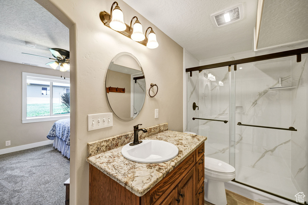 Bathroom with a textured ceiling, ceiling fan, vanity, a marble finish shower, and toilet