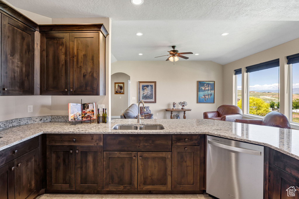 Kitchen with stainless steel dishwasher, a sink, a ceiling fan, dark brown cabinets, and light stone counters
