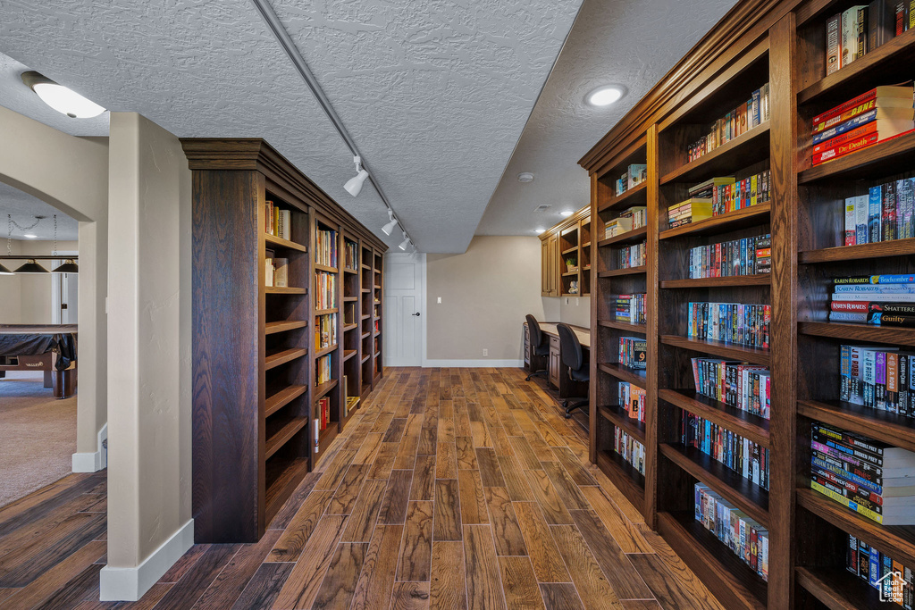 Hall with baseboards, dark wood-type flooring, a textured ceiling, arched walkways, and rail lighting