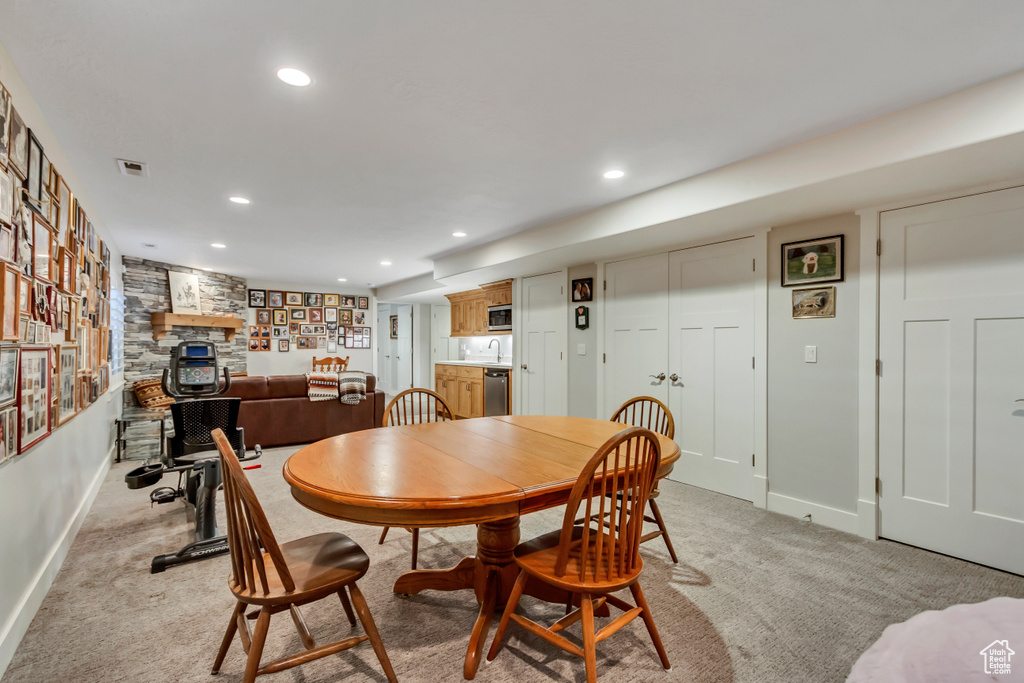 Dining area with baseboards, a stone fireplace, light carpet, and recessed lighting