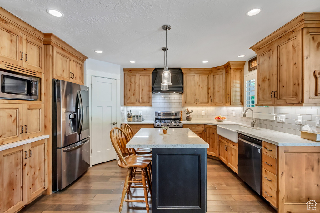 Kitchen with stainless steel appliances, custom range hood, a sink, hardwood / wood-style flooring, and a breakfast bar