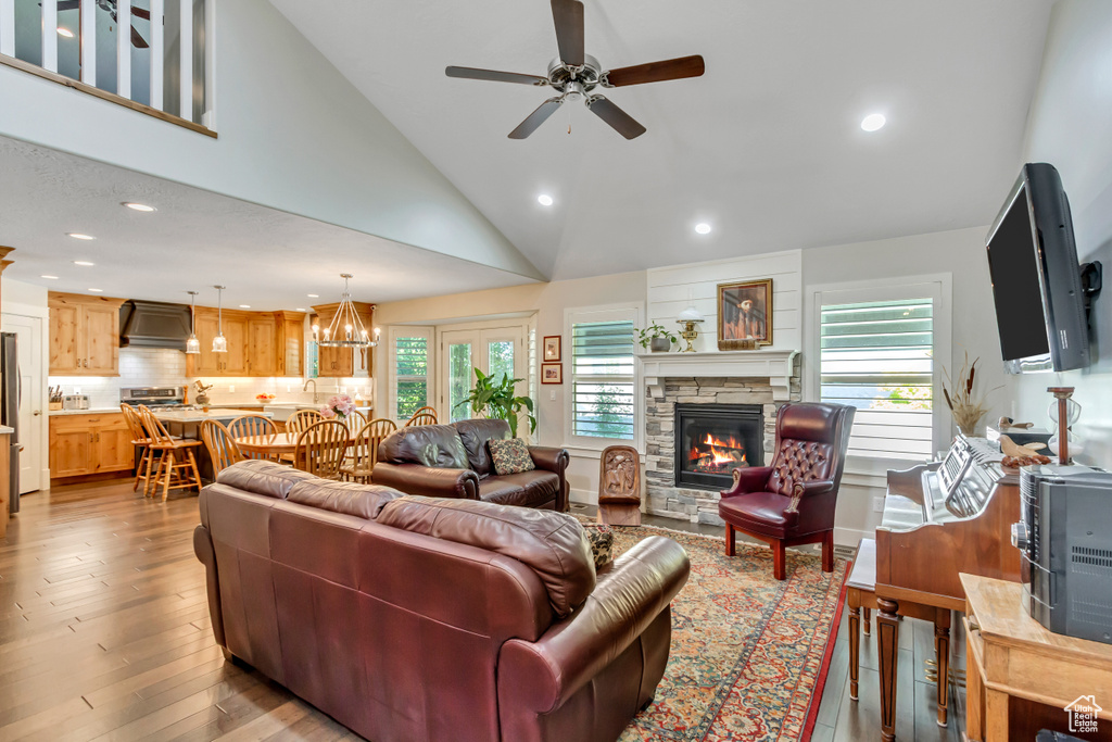 Living area featuring a ceiling fan, a stone fireplace, recessed lighting, wood finished floors, and a chandelier