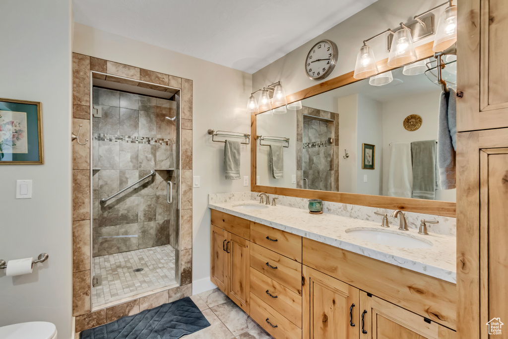 Full bathroom featuring double vanity, a shower stall, marble look tiles, and baseboards
