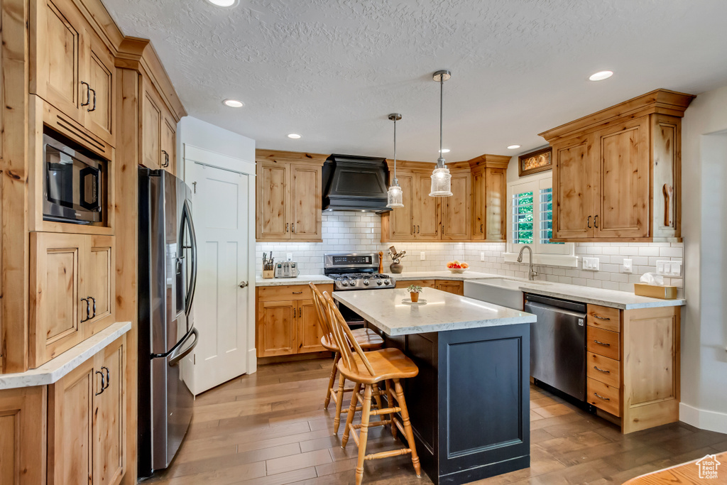Kitchen featuring stainless steel appliances, premium range hood, a sink, hardwood / wood-style floors, and a kitchen island