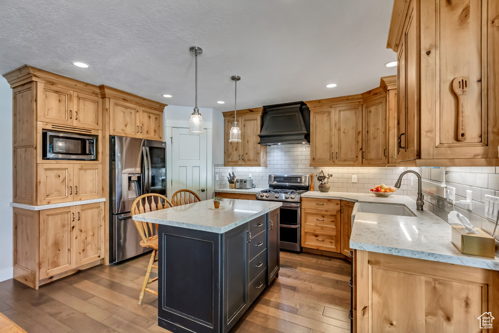 Kitchen with appliances with stainless steel finishes, premium range hood, a sink, hardwood / wood-style floors, and recessed lighting
