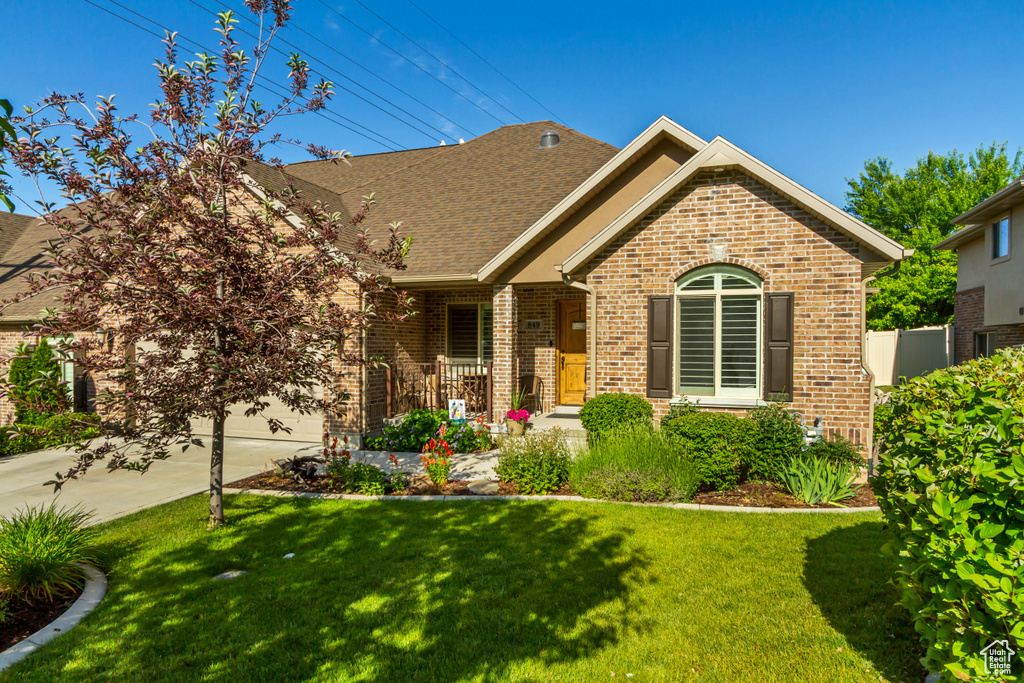View of front of home with brick siding, driveway, a front lawn, and roof with shingles