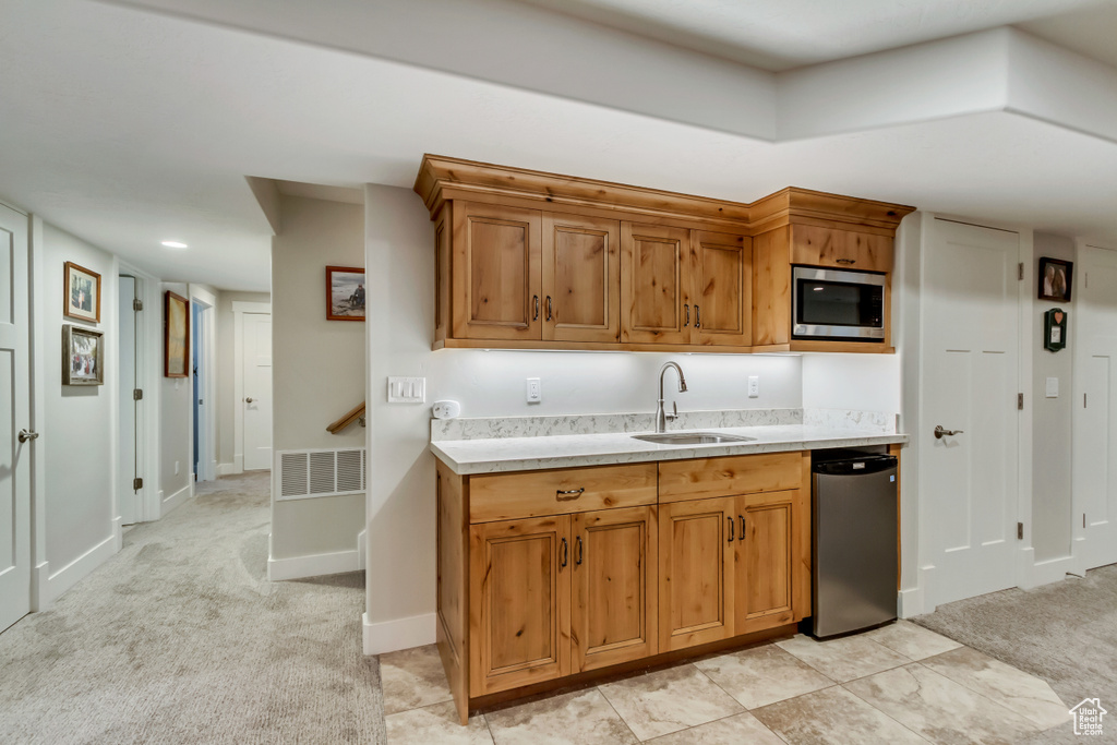 Kitchen with a sink, stainless steel microwave, light countertops, light carpet, and brown cabinets