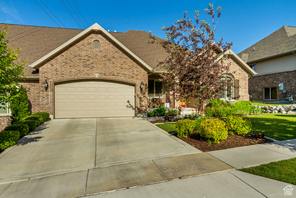 View of front facade featuring brick siding, an attached garage, driveway, and roof with shingles