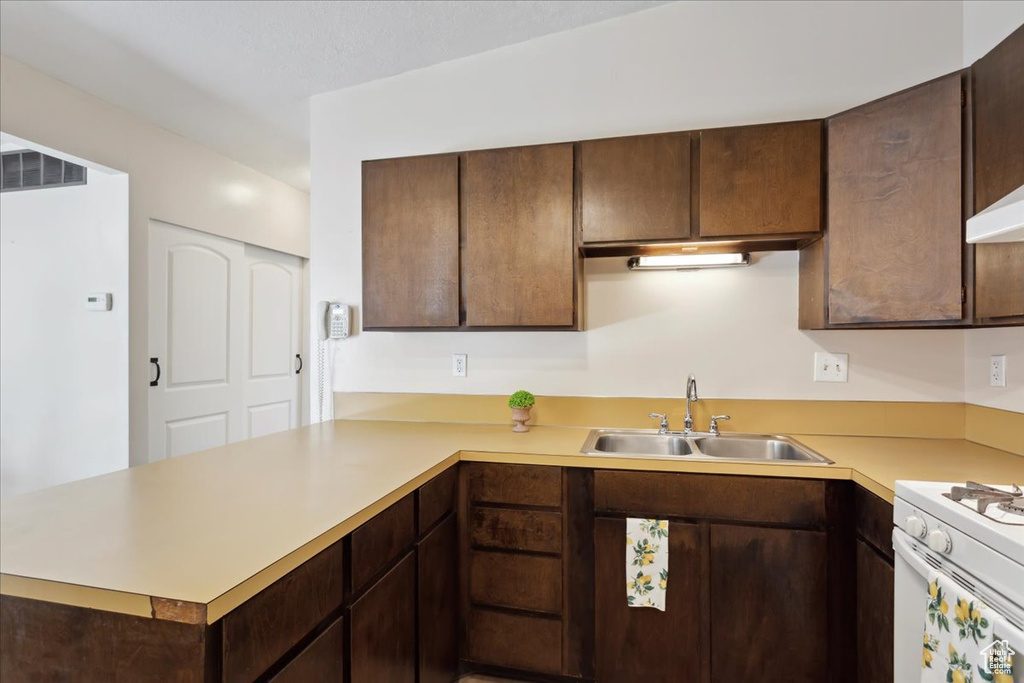Kitchen with a sink, a peninsula, light countertops, and dark brown cabinets