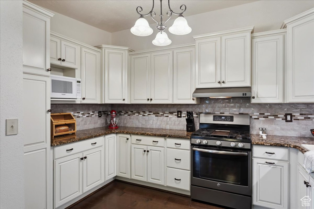 Kitchen featuring stainless steel gas stove, under cabinet range hood, a chandelier, white microwave, and tasteful backsplash