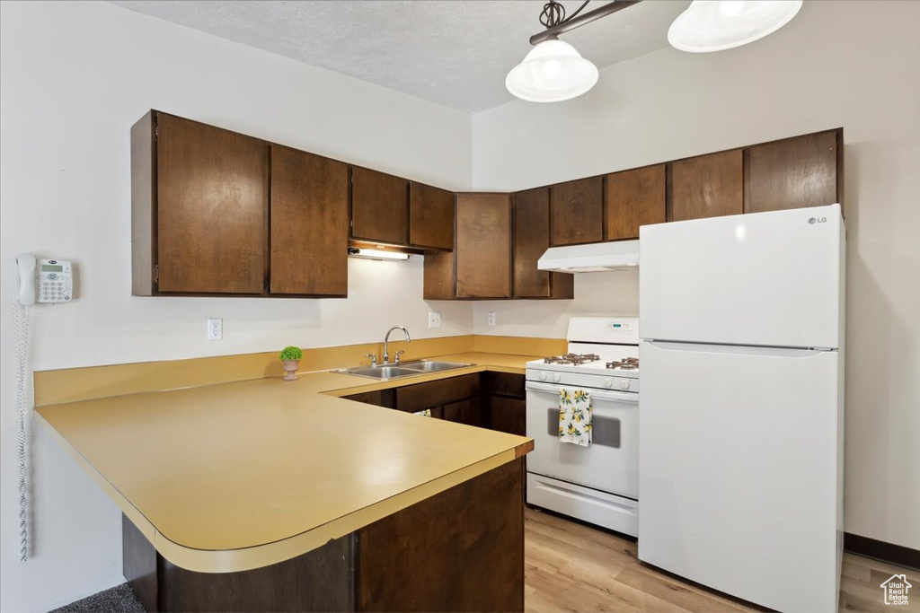 Kitchen featuring white appliances, under cabinet range hood, a sink, light countertops, and a peninsula