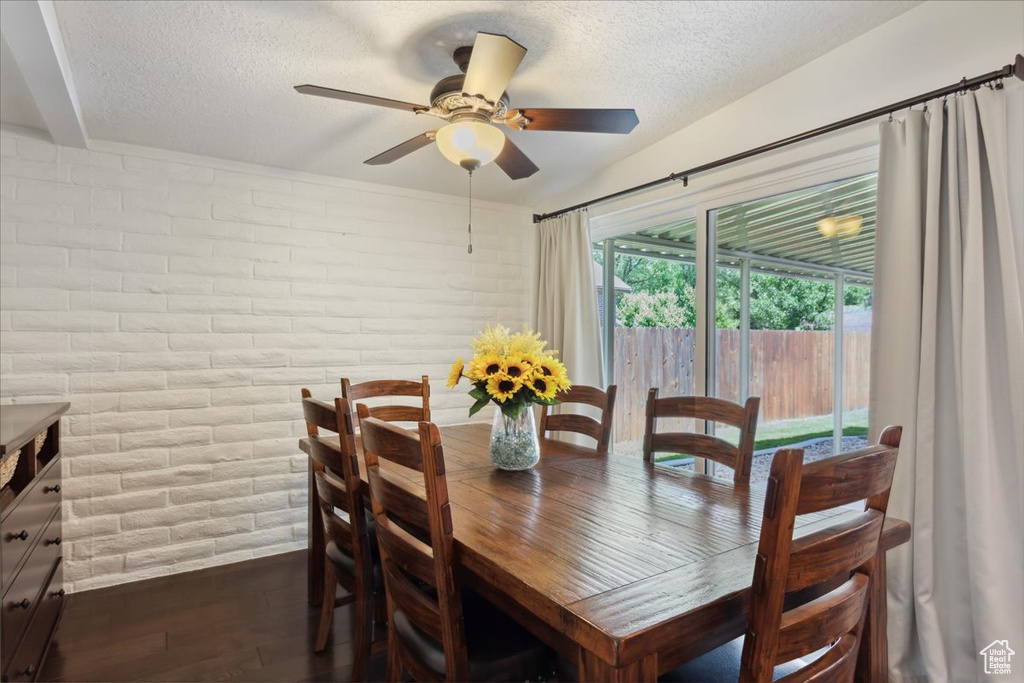 Dining room featuring a textured ceiling, dark wood-type flooring, a ceiling fan, brick wall, and baseboards