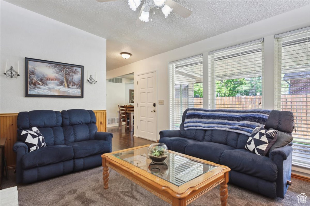 Living room featuring a textured ceiling, a wainscoted wall, a ceiling fan, wood walls, and carpet flooring