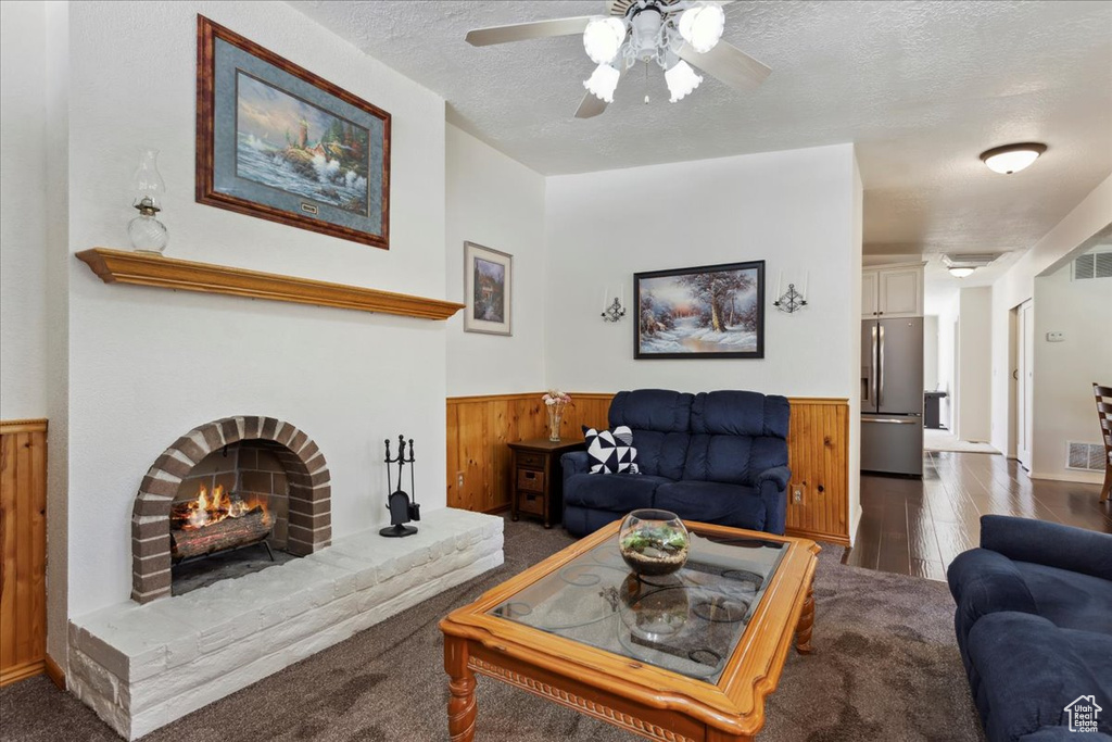 Living room featuring a wainscoted wall, ceiling fan, a fireplace, a textured ceiling, and wood walls
