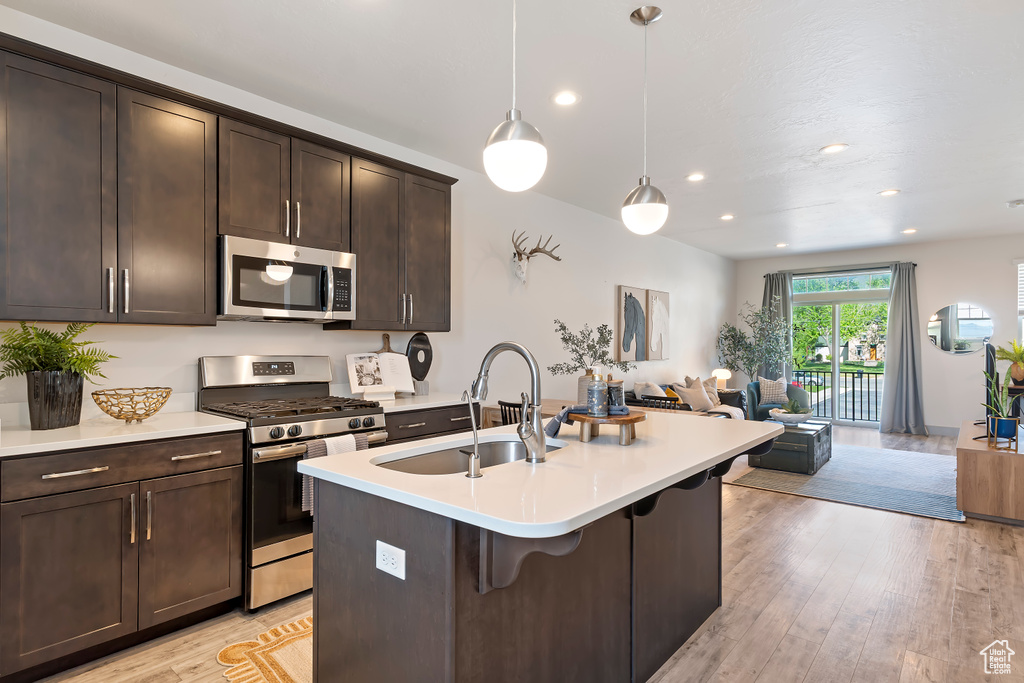 Kitchen featuring appliances with stainless steel finishes, a sink, open floor plan, light countertops, and dark brown cabinets