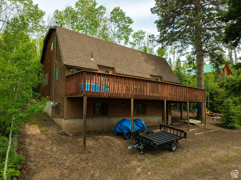 Rear view of house featuring a shingled roof, a deck, and a gambrel roof