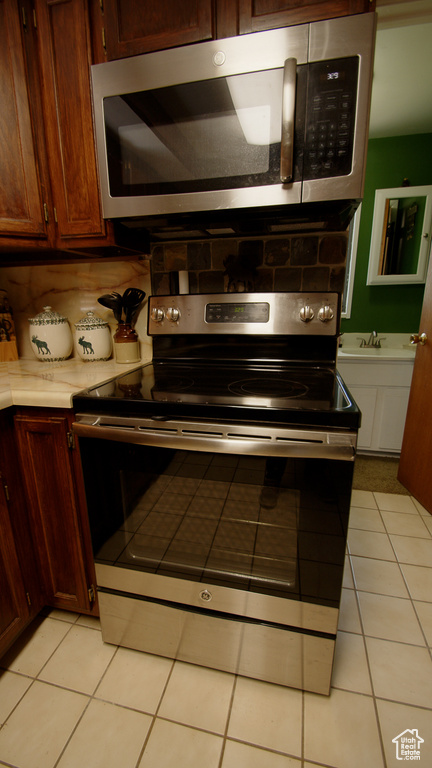 Kitchen with stainless steel appliances, light tile patterned flooring, tasteful backsplash, light countertops, and a sink