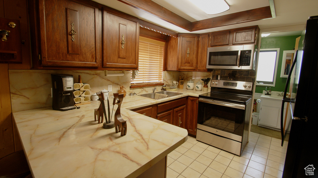 Kitchen with appliances with stainless steel finishes, a sink, light countertops, a peninsula, and tasteful backsplash